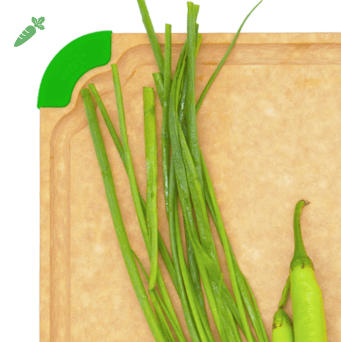 Close-up of an Elihome wood fiber cutting board featuring a juice groove and a green non-slip silicone corner for vegetables, shown with scallions and pepper.