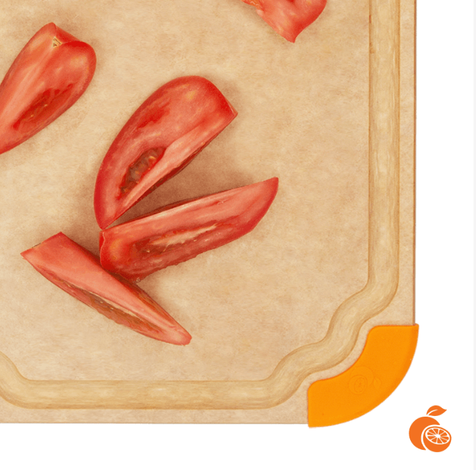 Close-up of an Elihome wood fiber cutting board featuring a juice groove and an orange non-slip silicone corner, shown with sliced tomatoes.