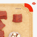 Close-up of an Elihome wood fiber cutting board with color-coded red silicone corner for meat and seafood, featuring juice groove, shown with raw beef and garlic.