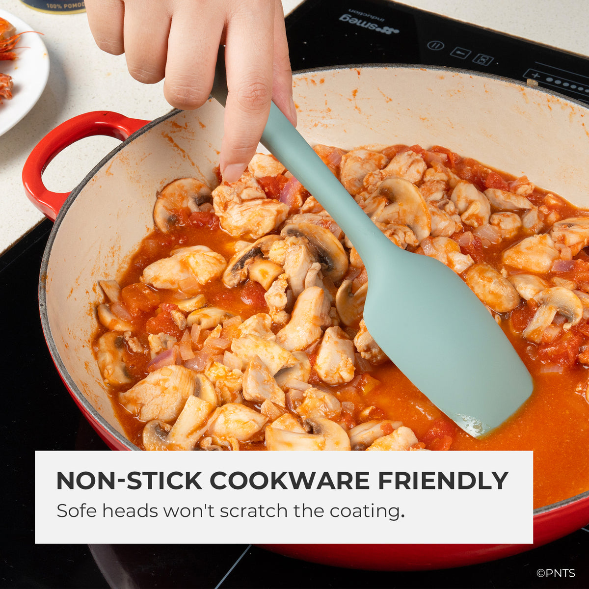 Person stirring a dish of chicken and mushrooms in a red pot with a green spatula, text indicating non-stick cookware compatibility.