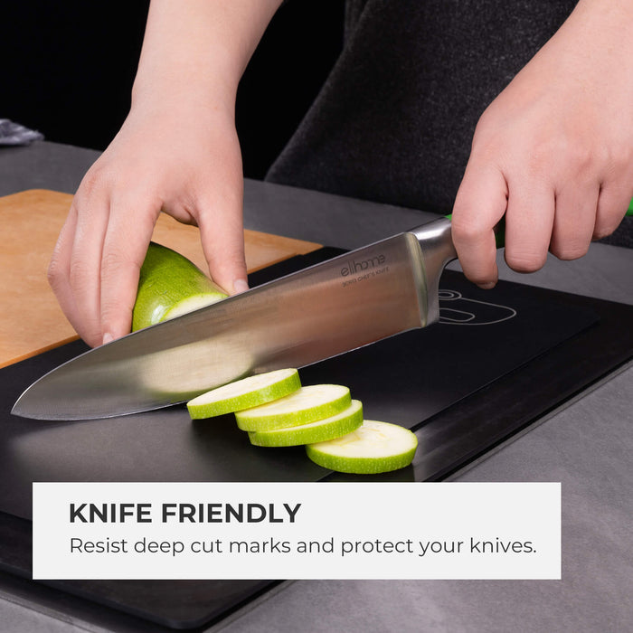 Close-up of a chef's knife slicing zucchini on an Elihome black wood fiber cutting board, demonstrating the surface quality. Text reads: "Knife Friendly. Resist deep cut marks and protect your knives."