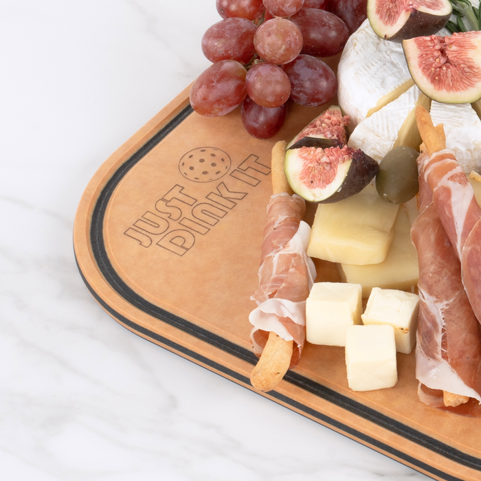 Fresh figs, prosciutto, brie, aged cheese, and grapes served on an Elihome pickleball paddle board engraved with Just Dink It